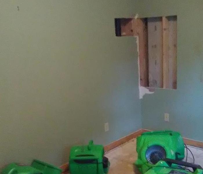 Wall with a wall cut and green air movers on the floor. 