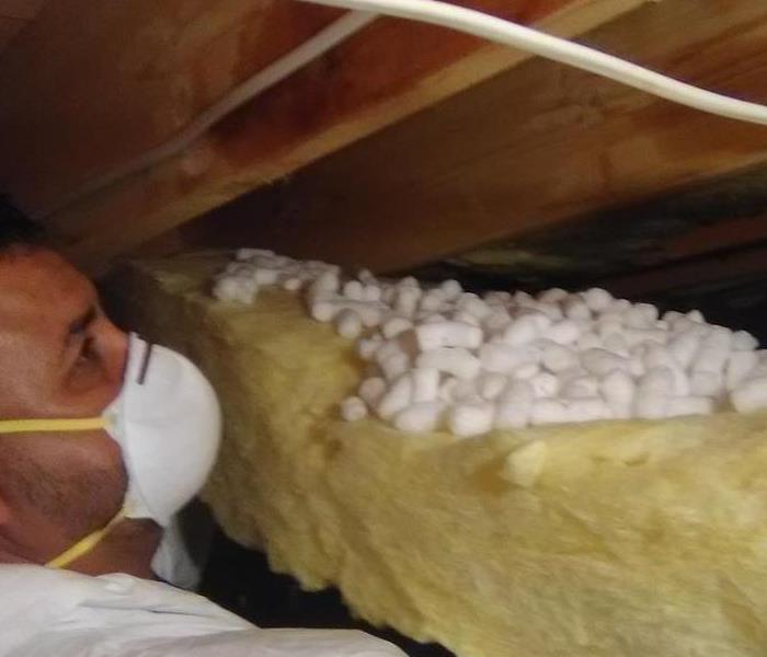Team member dressed in white protective gear next to yellow insulation