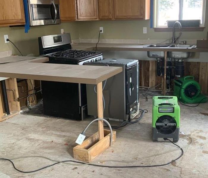 Cabinet doors are missing with green air movers on the ground. 